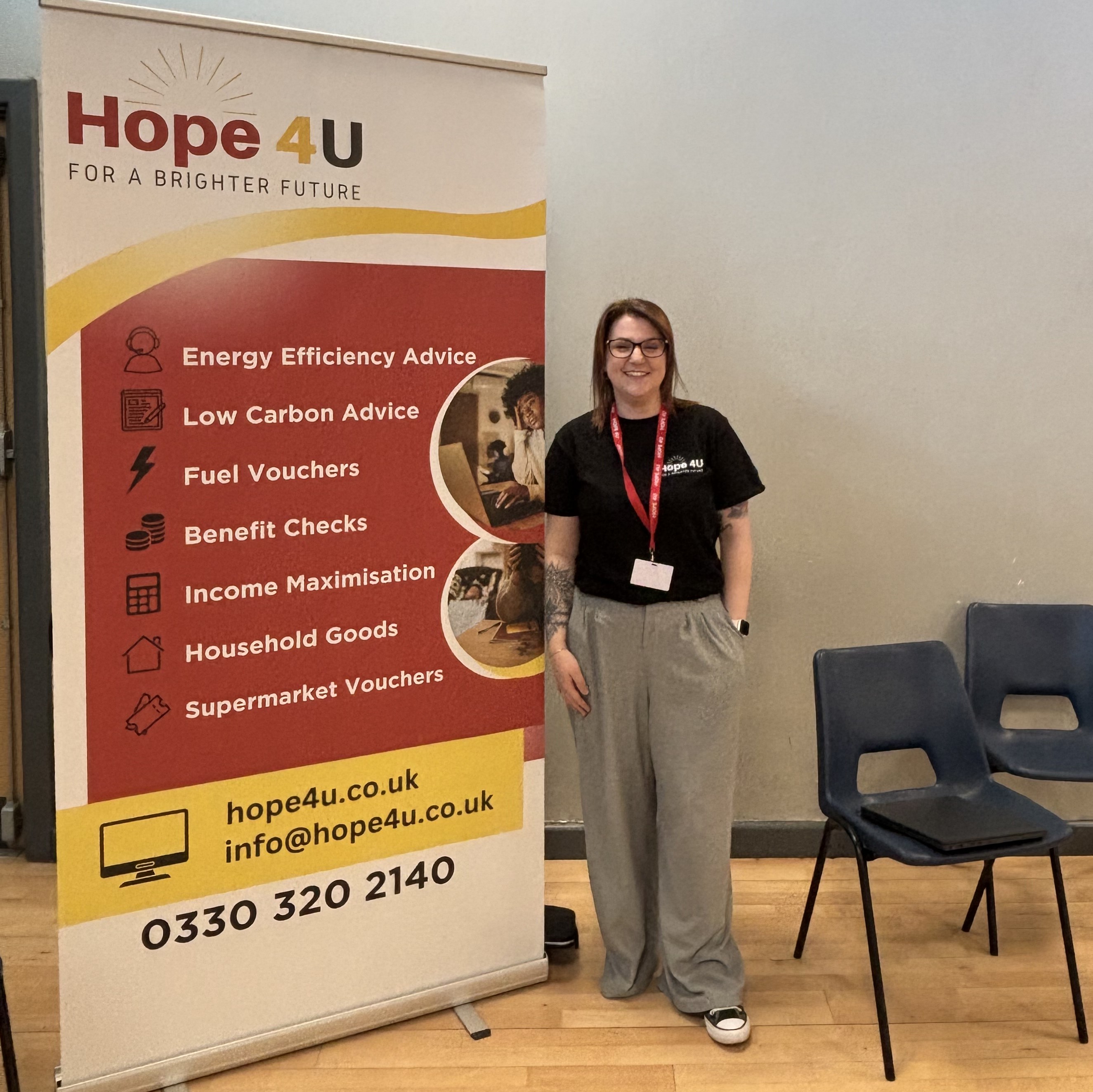 A smiling person stands beside a "Hope 4U" banner listing services like energy advice and vouchers. The setting is informal and welcoming.