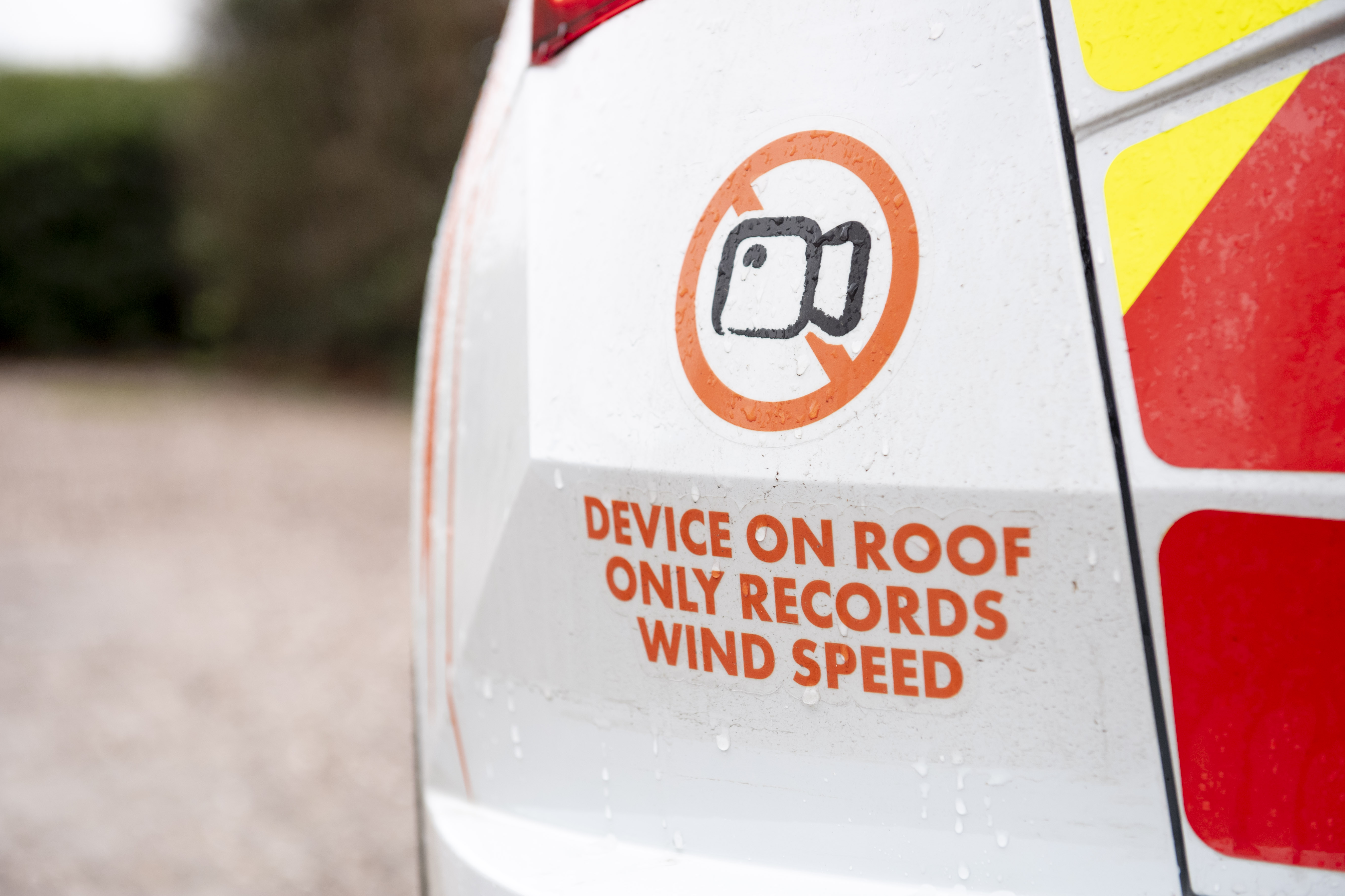 Side view of a white Cadent gas network vehicle with orange branding and roof-mounted monitoring equipment parked on gravel
