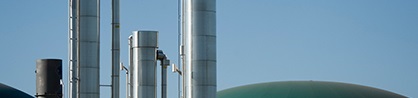 Metallic industrial chimneys rise against a clear blue sky. Rounded green storage domes are visible, suggesting a modern industrial facility.