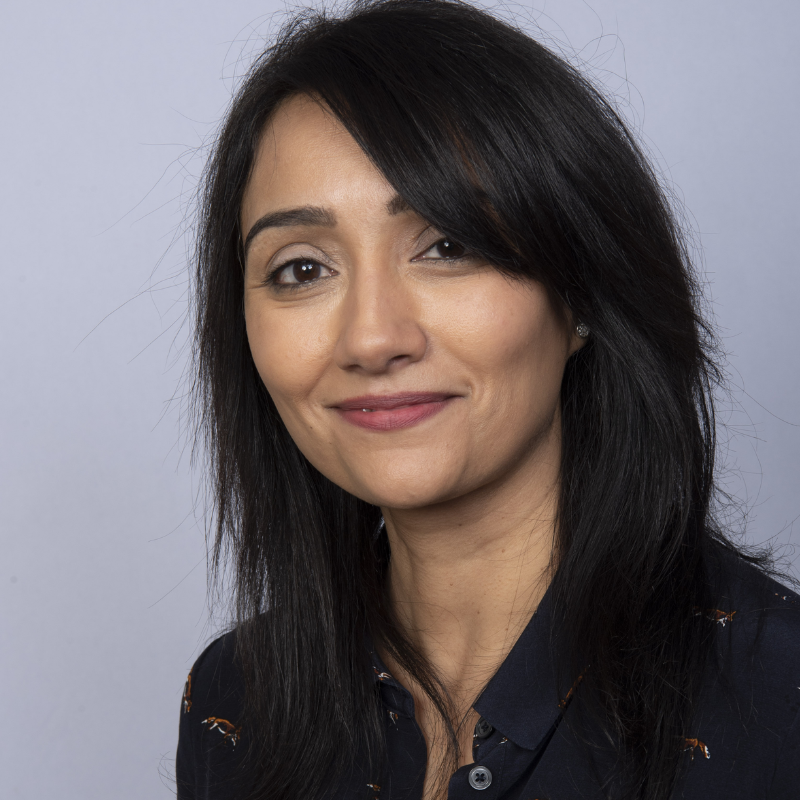 A woman with long black hair smiles slightly against a plain gray background. She wears a dark shirt with small fox motifs, conveying a calm and professional demeanor.