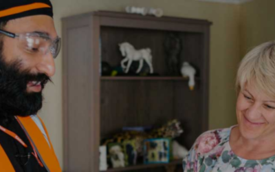 A utility worker wearing safety glasses and a high-visibility vest talks with a smiling woman inside her home.