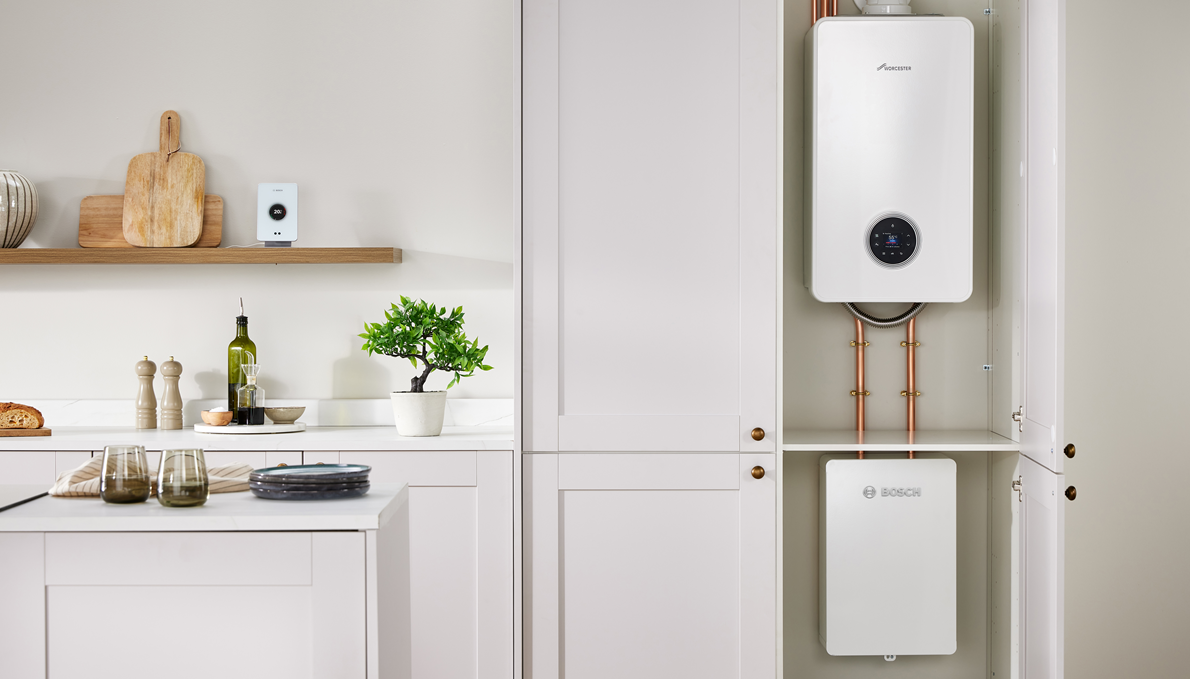Hybrid heating system installed in a kitchen cupboard showing a Worcester Bosch boiler and indoor unit connected by copper pipes.