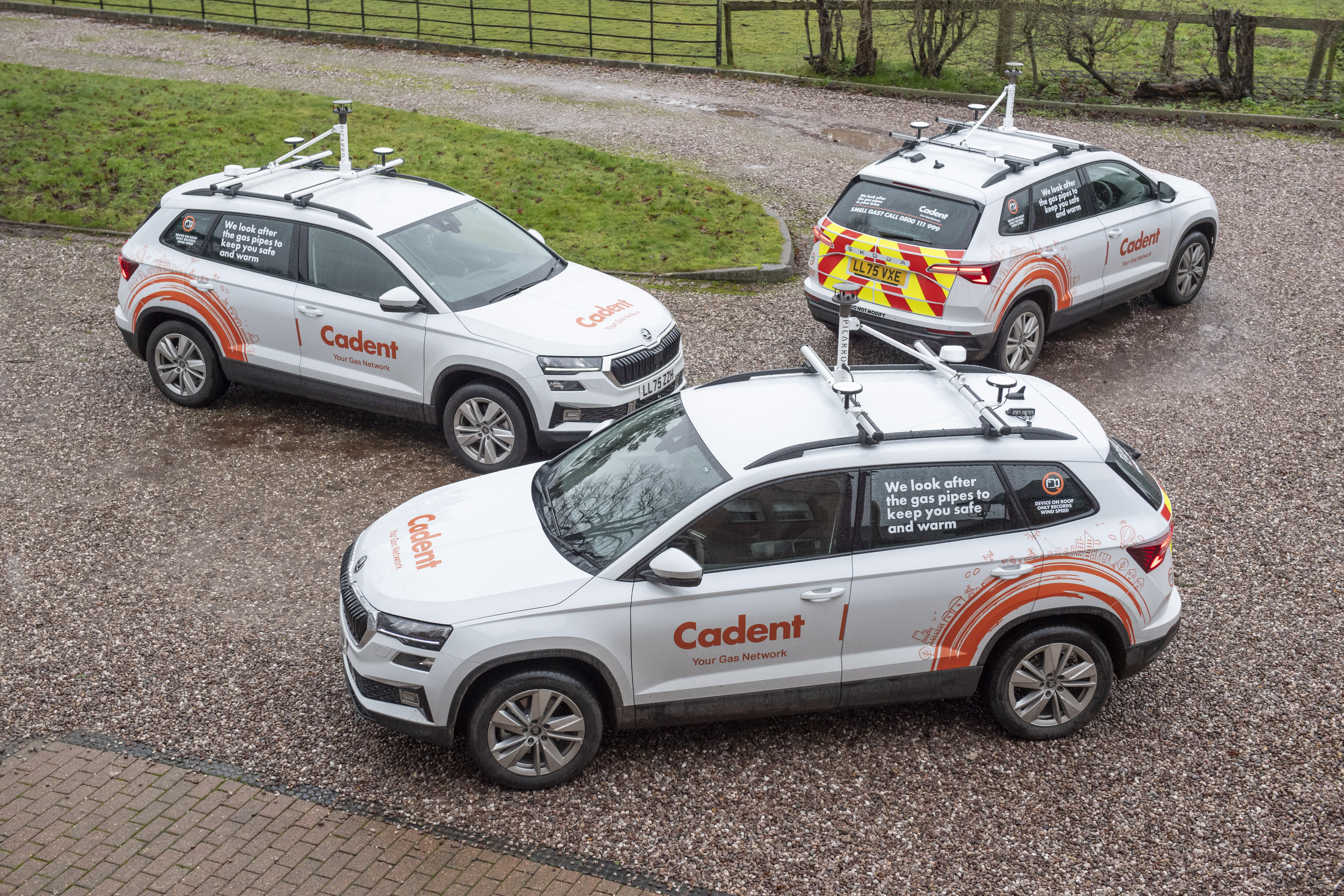 Three Cadent gas network vehicles parked on a gravel area, each fitted with roof-mounted monitoring equipment used to detect gas leaks