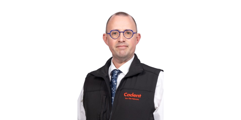 A person wearing a black Cadent vest with a white shirt and patterned blue tie stands against a plain white background, conveying a professional demeanor.