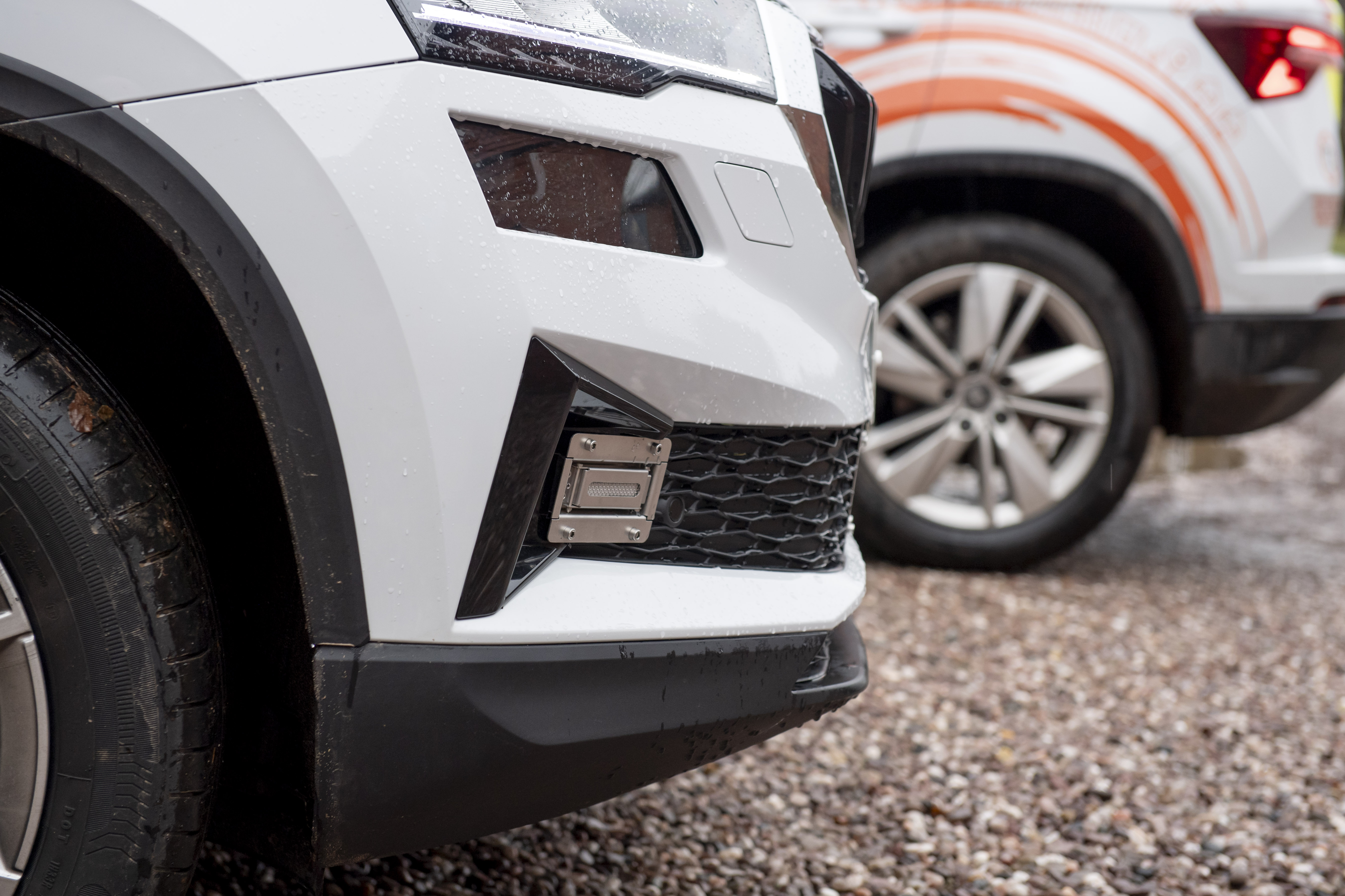 Close-up of the front bumper of a Cadent vehicle showing a mounted sensor device near the grille