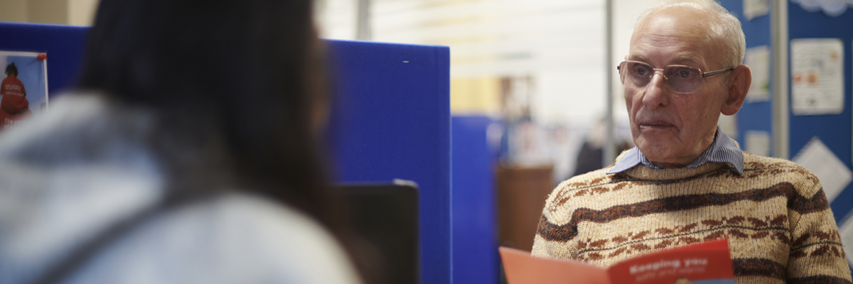 An older adult male discusses information from a leaflet during a one-to-one support session.