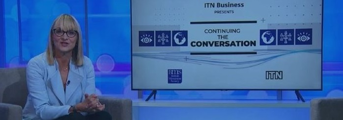 A woman in a light blue blazer sits on a chair in a studio setting. Beside her, a screen displays "ITN Business presents CONTINUING THE CONVERSATION.