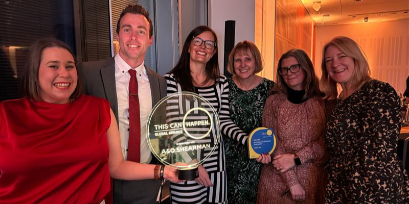 A group of people standing, smiling, and posing for a photoshoot, with a glass trophy and another trophy on hands.