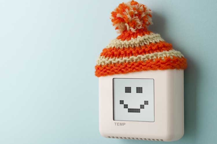 Digital thermostat with a smiling face display, wearing a knitted orange and cream winter hat