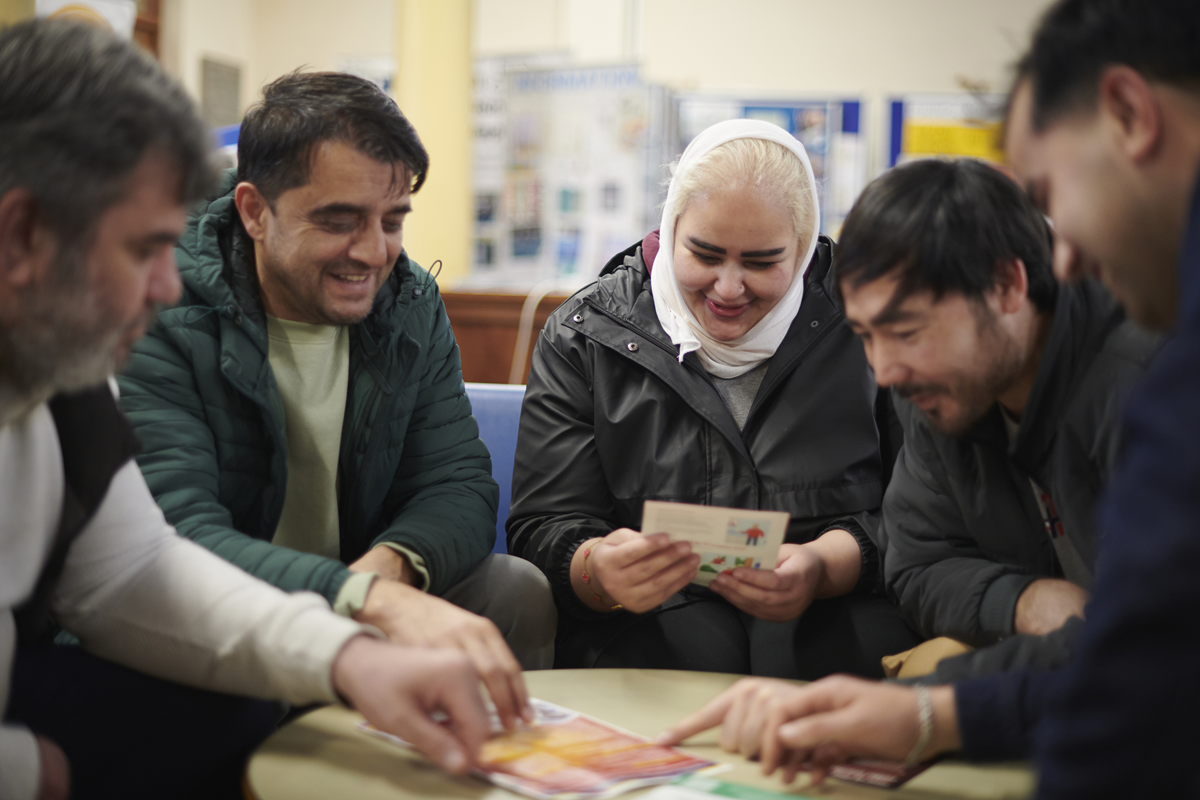 A group of adults sit around a table, looking at printed materials during a community discussion session.