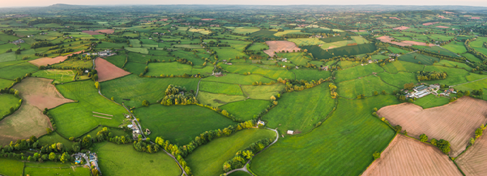 Green fields and farmland seen from above, with hedgerows, country roads and scattered farm buildings
