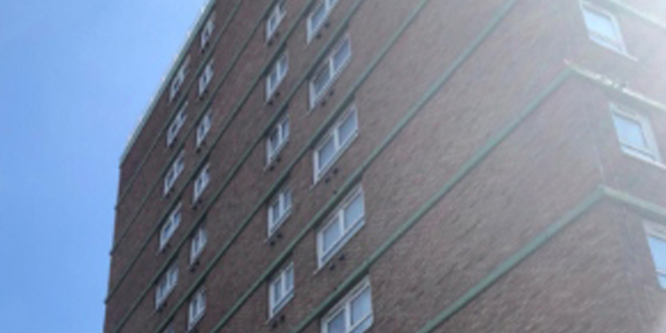 Tall brick apartment building with multiple rows of windows against a clear blue sky