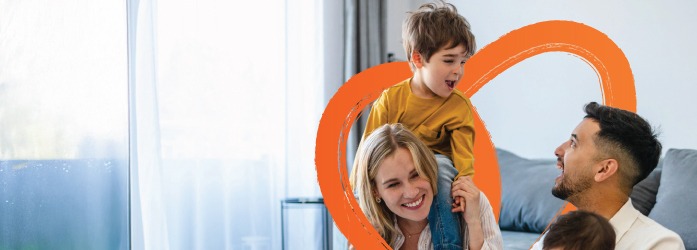 A family sitting together on a couch at home, with one child sitting on an adult’s shoulders.
