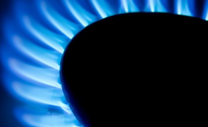 Close-up of a blue gas flame on a stove, partially obscured by a dark pot. The flame glows intensely, creating a warm and vibrant atmosphere.