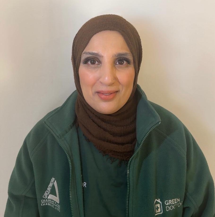 A woman smiles warmly at the camera, wearing a green jacket with 