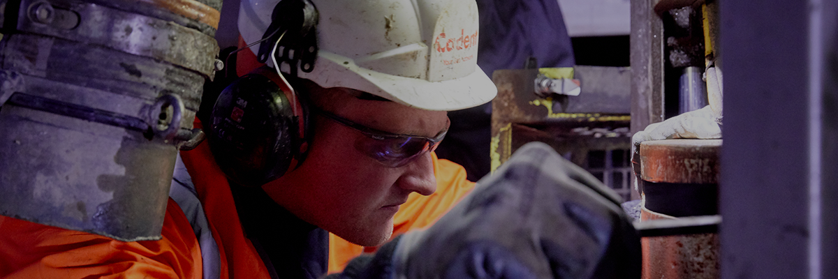 Engineer wearing Cadent hard hat and ear defenders, in an engineering environment fixing pipe at night