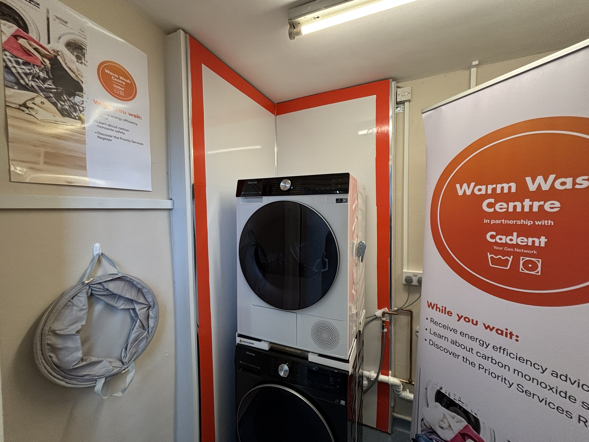 Compact laundry room featuring stacked washer-dryer, red and white panels, posters about energy efficiency, and a laundry basket.