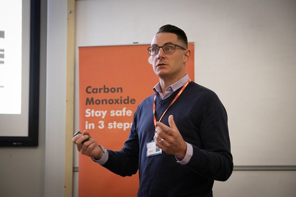 Person giving a presentation on carbon monoxide safety with an orange safety poster in the background